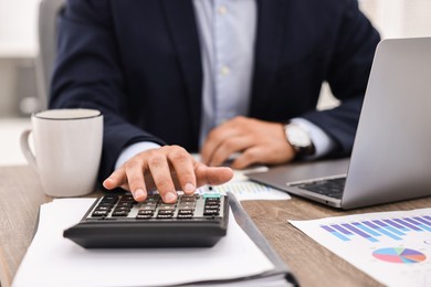 Banker using calculator at wooden table in office, closeup