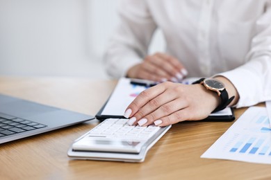 Banker using calculator at wooden table in office, closeup