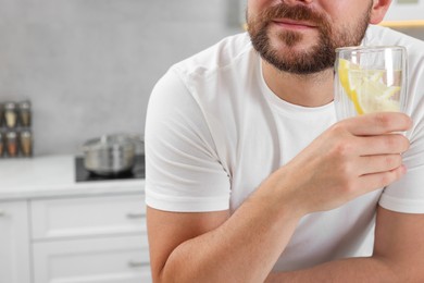 Man holding glass of water with lemon in kitchen, closeup. Space for text