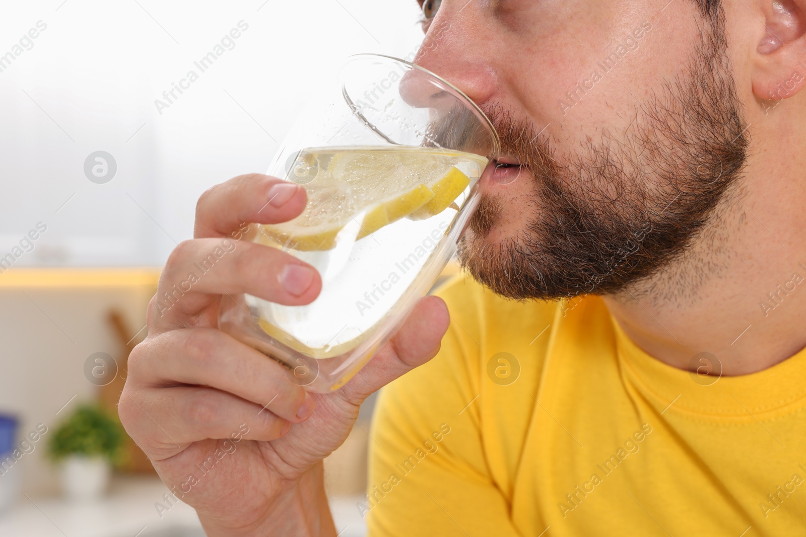 Photo of Man drinking water with lemon indoors, closeup