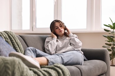 Loneliness concept. Sad teenage girl in headphones listening to music on sofa at home