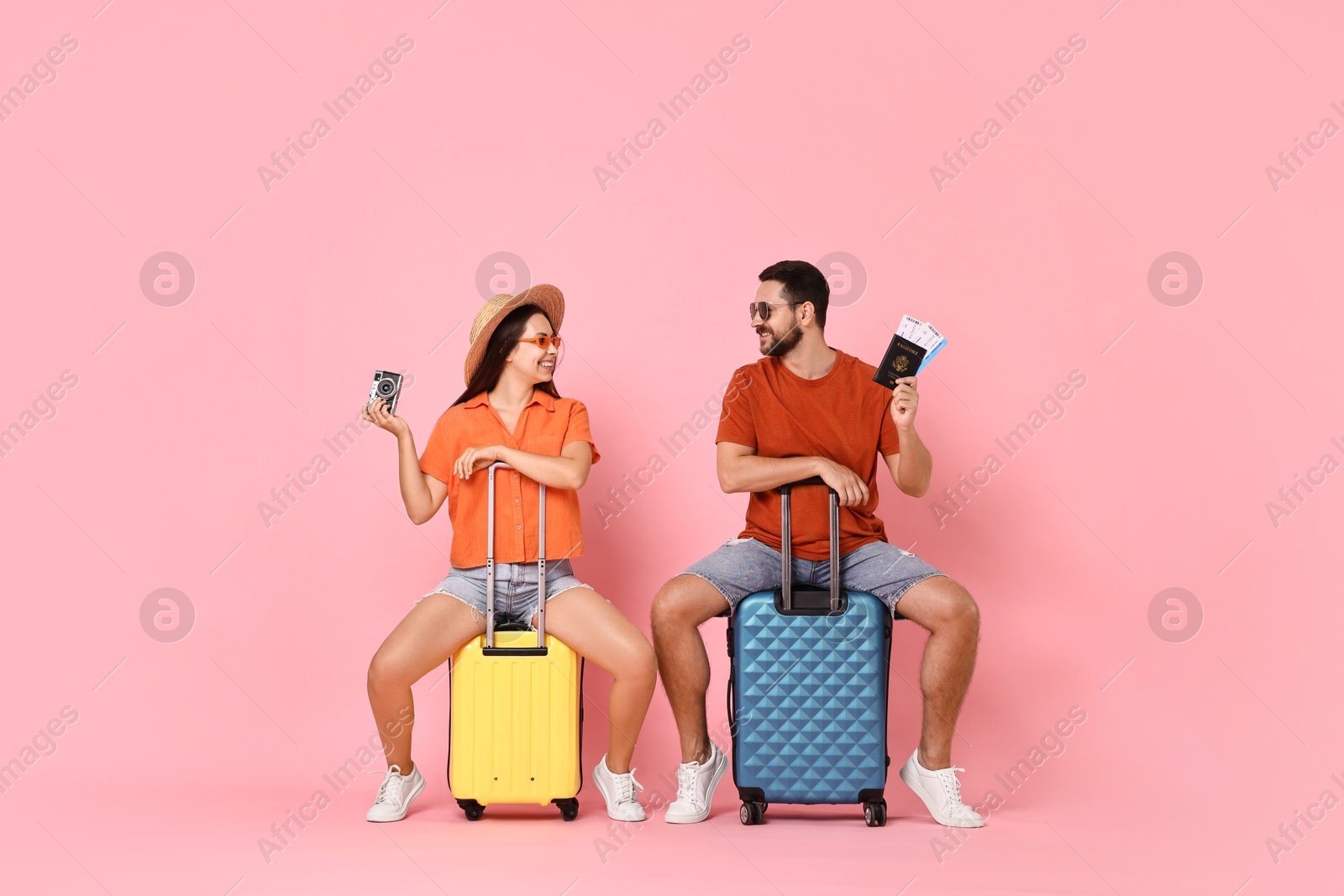 Photo of Happy couple with suitcases, passport, tickets and vintage camera on pink background