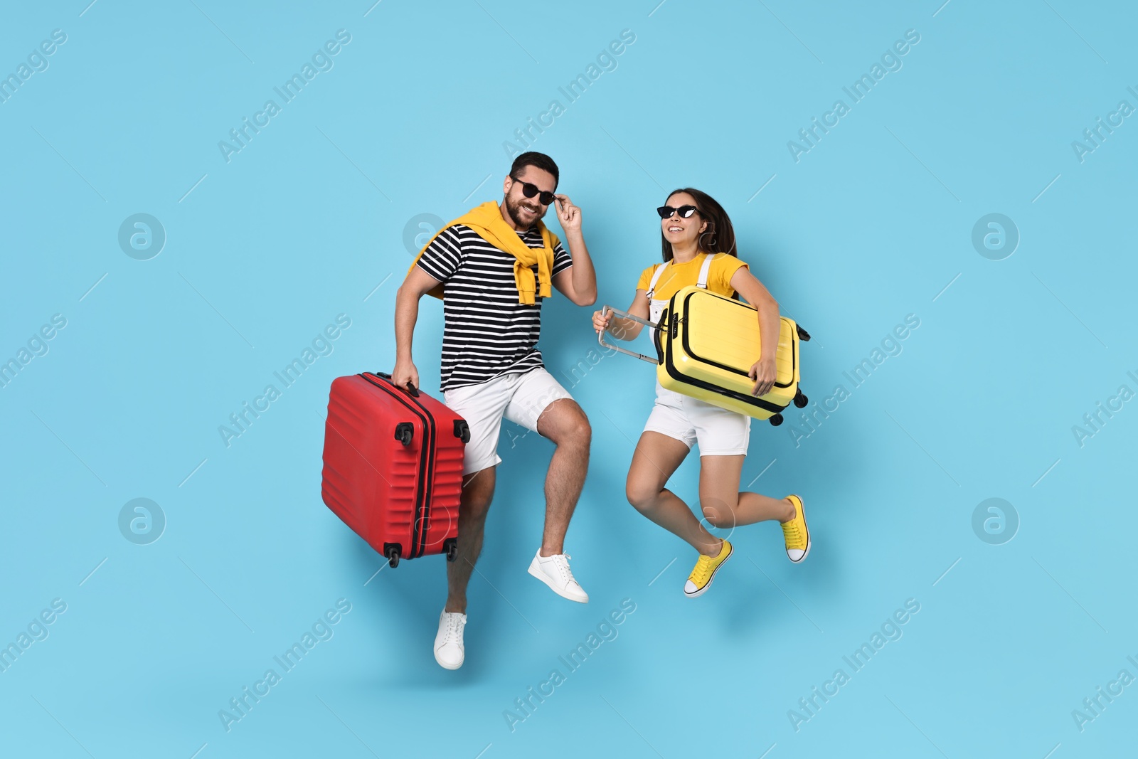 Photo of Happy couple in sunglasses with suitcases jumping on light blue background