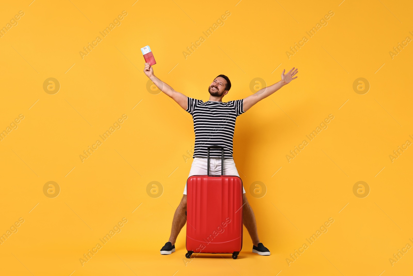 Photo of Happy man with passport, ticket and suitcase on orange background