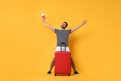 Happy man with passport, ticket and suitcase on orange background