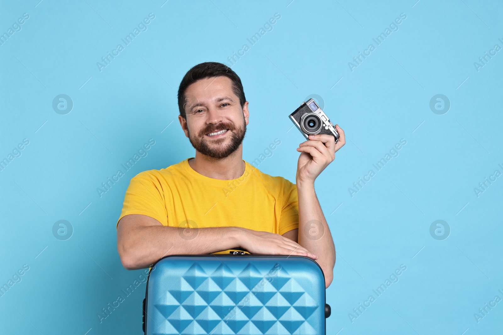 Photo of Happy man with suitcase and vintage camera on light blue background