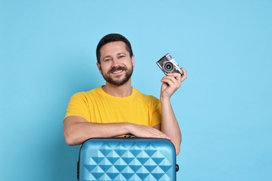 Photo of Happy man with suitcase and vintage camera on light blue background