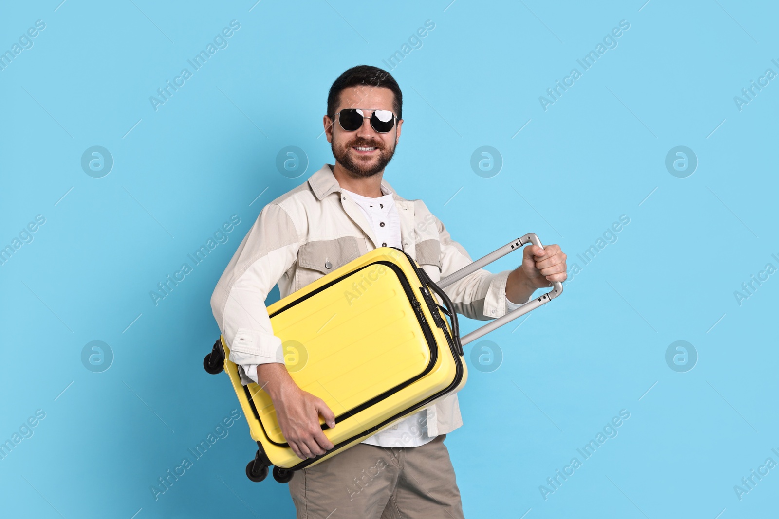 Photo of Happy man in sunglasses with suitcase on light blue background