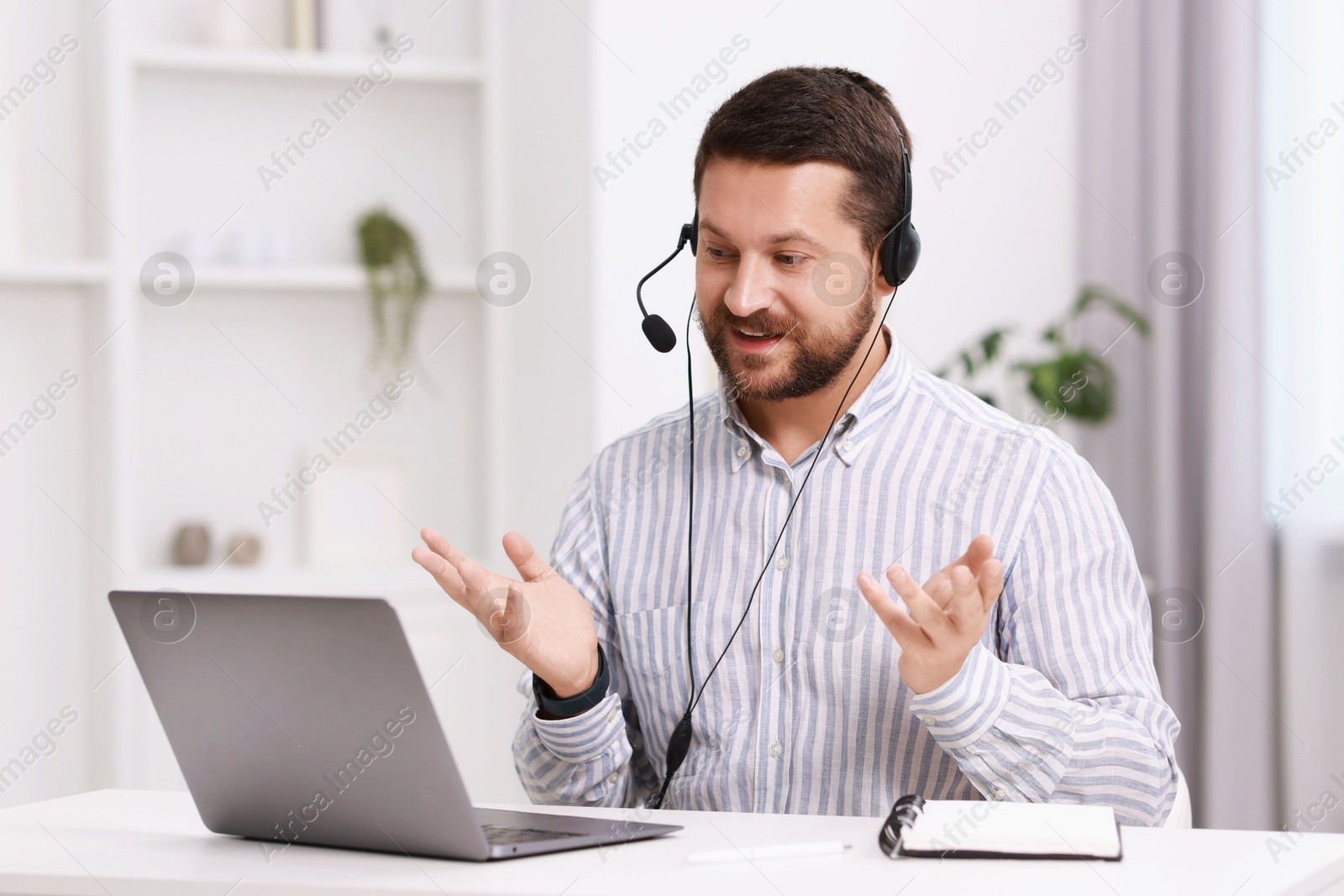 Photo of Interpreter in headset having video chat via laptop at white table indoors