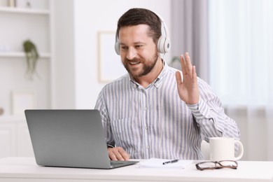 Interpreter in headphones having video chat via laptop at white table indoors