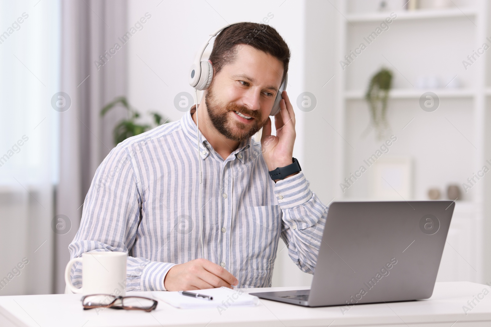 Photo of Interpreter in headphones having video chat via laptop at white table indoors