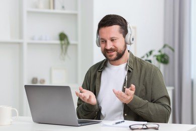 Interpreter in headphones having video chat via laptop at white table indoors