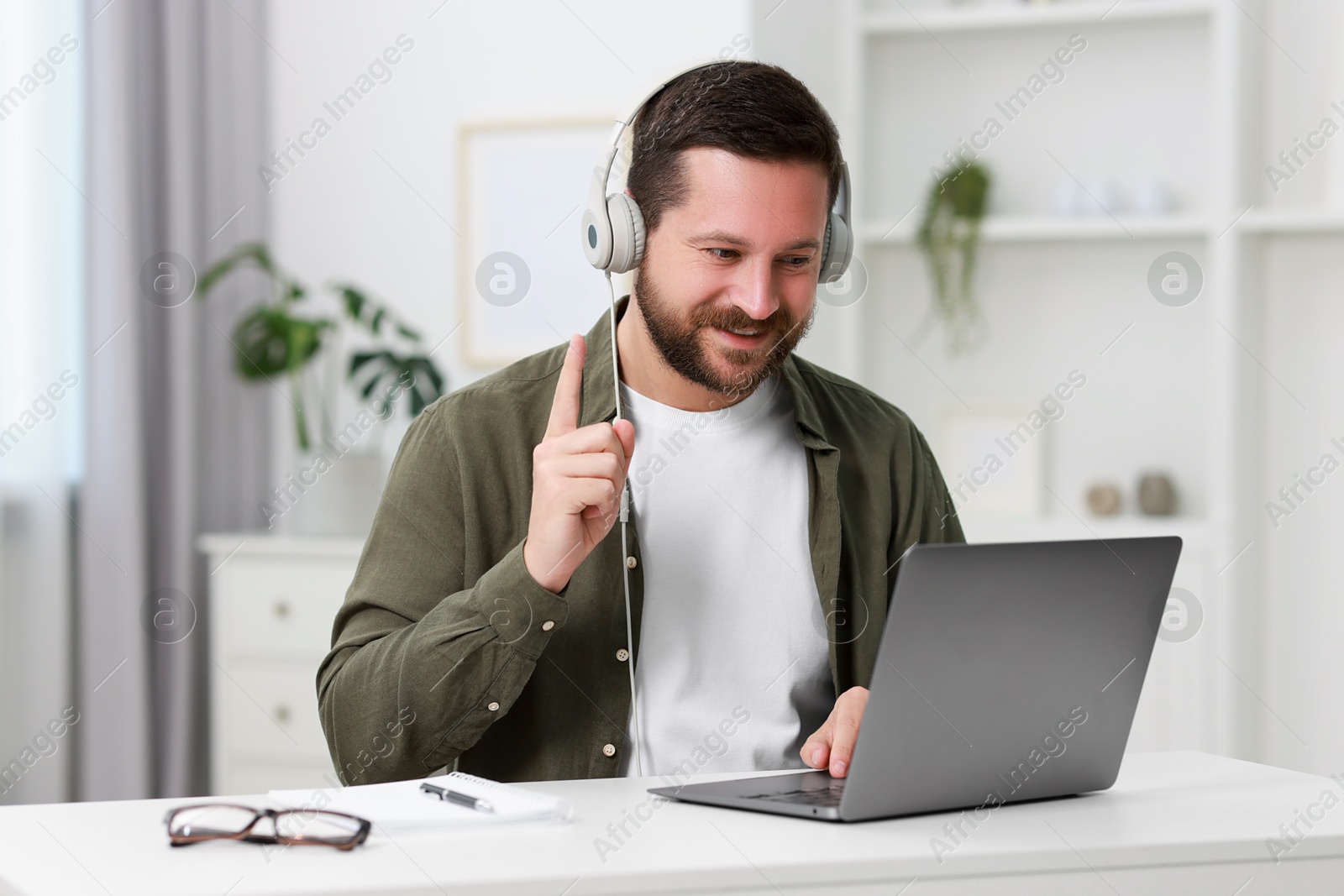 Photo of Interpreter in headphones having video chat via laptop at white table indoors