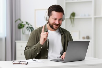 Interpreter in headphones having video chat via laptop at white table indoors