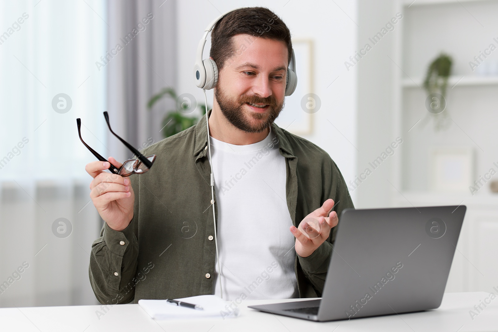 Photo of Interpreter in headphones having video chat via laptop at white table indoors