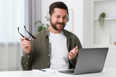 Interpreter in headphones having video chat via laptop at white table indoors