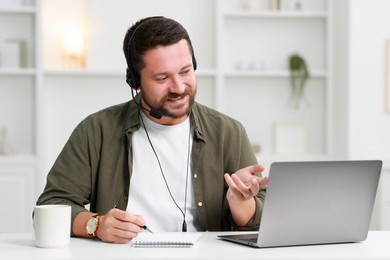 Interpreter in headset taking notes while having video chat via laptop at white table indoors