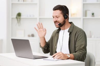 Interpreter in headset having video chat via laptop at white table indoors