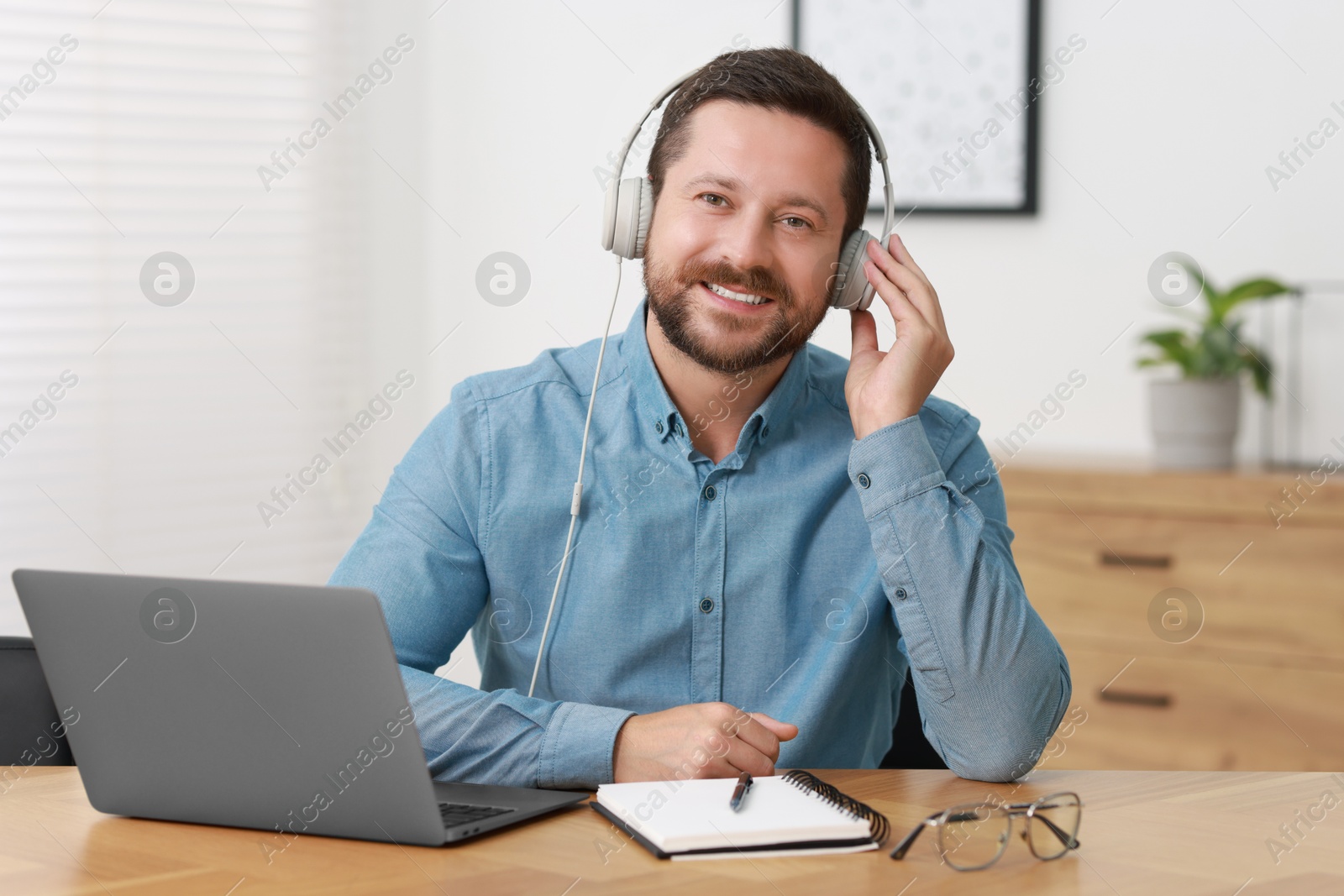 Photo of Interpreter in headphones having video chat via laptop at wooden table indoors