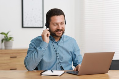 Interpreter in headset having video chat via laptop at wooden table indoors