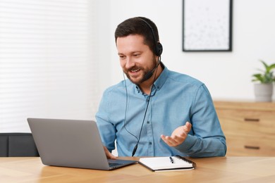 Photo of Interpreter in headset having video chat via laptop at wooden table indoors