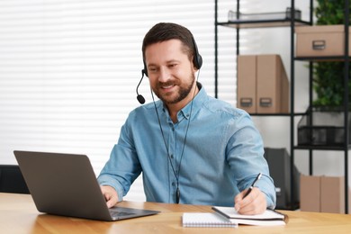 Interpreter in headset taking notes while having video chat via laptop at wooden table indoors