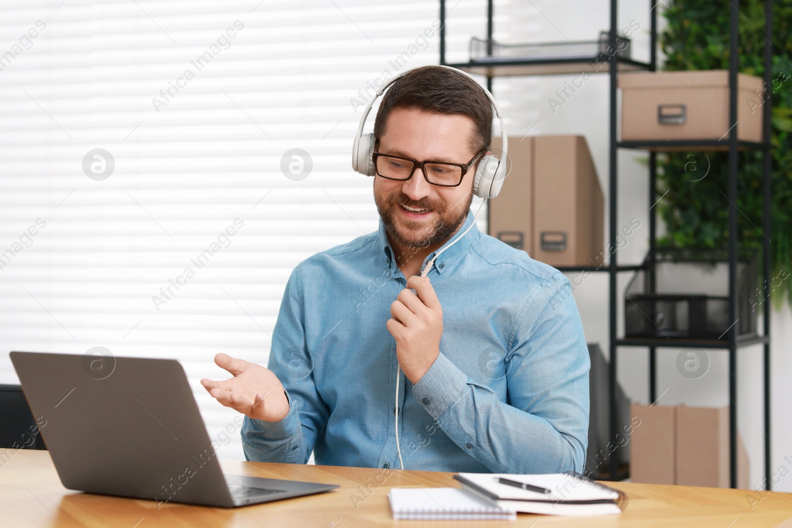 Photo of Interpreter in headphones having video chat via laptop at wooden table indoors