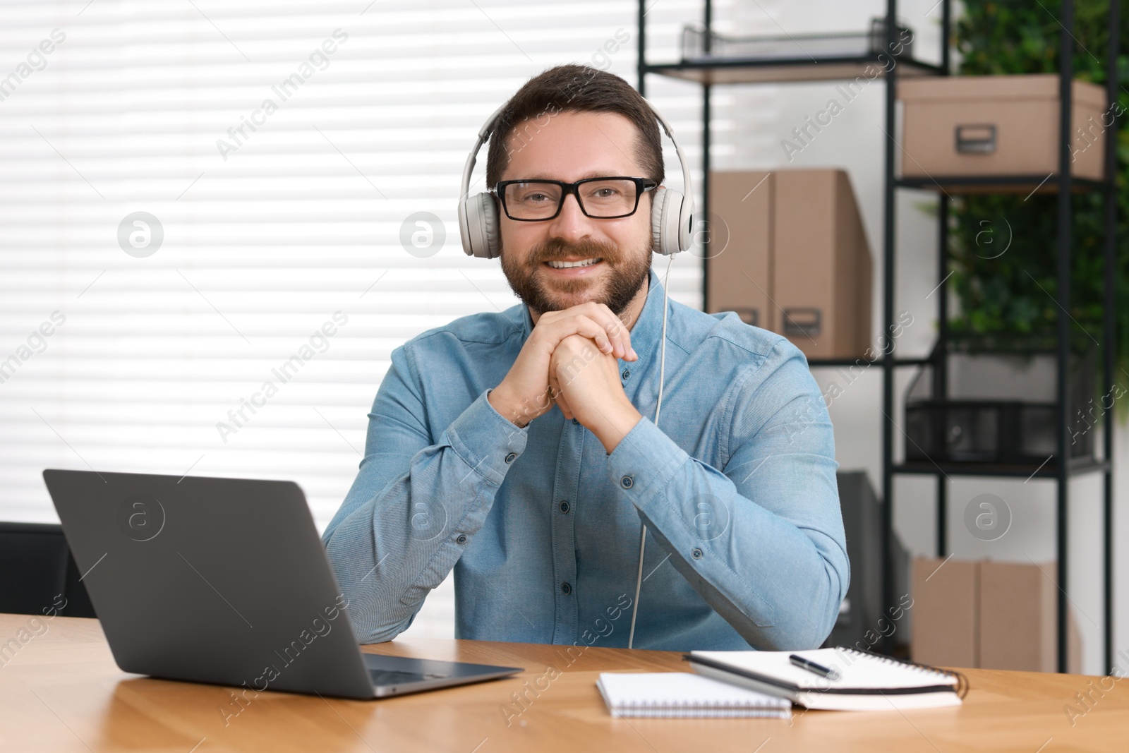 Photo of Interpreter in headphones having video chat via laptop at wooden table indoors