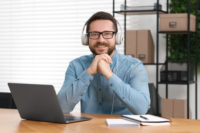 Interpreter in headphones having video chat via laptop at wooden table indoors