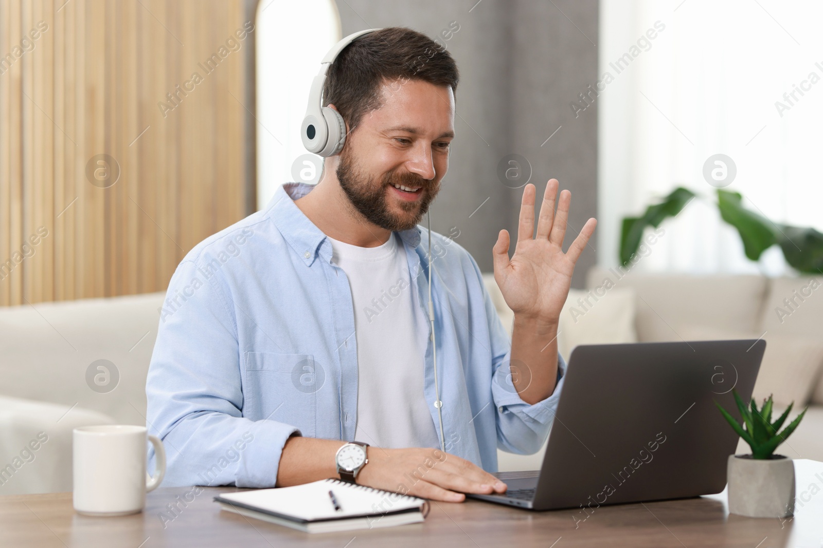 Photo of Interpreter in headphones having video chat via laptop at wooden table indoors