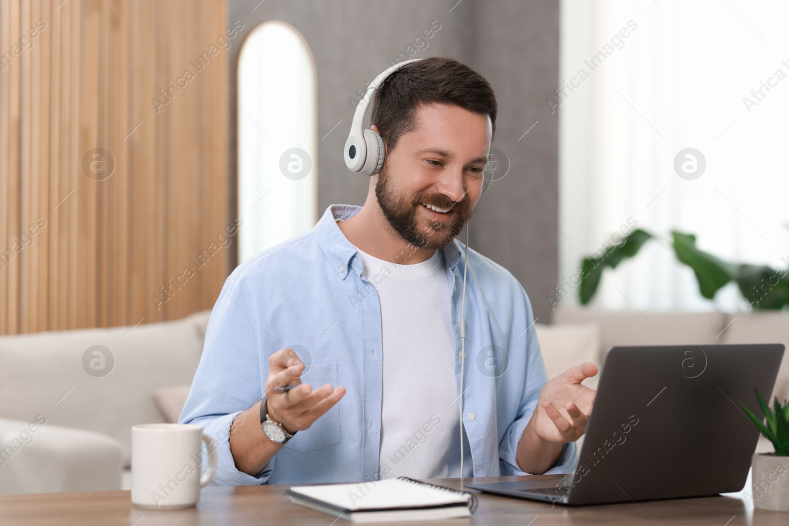 Photo of Interpreter in headphones having video chat via laptop at wooden table indoors