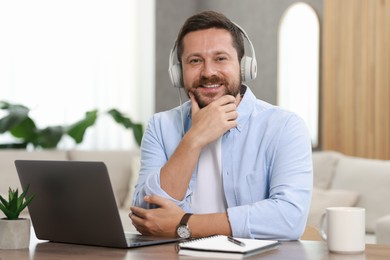 Photo of Interpreter in headphones having video chat via laptop at wooden table indoors