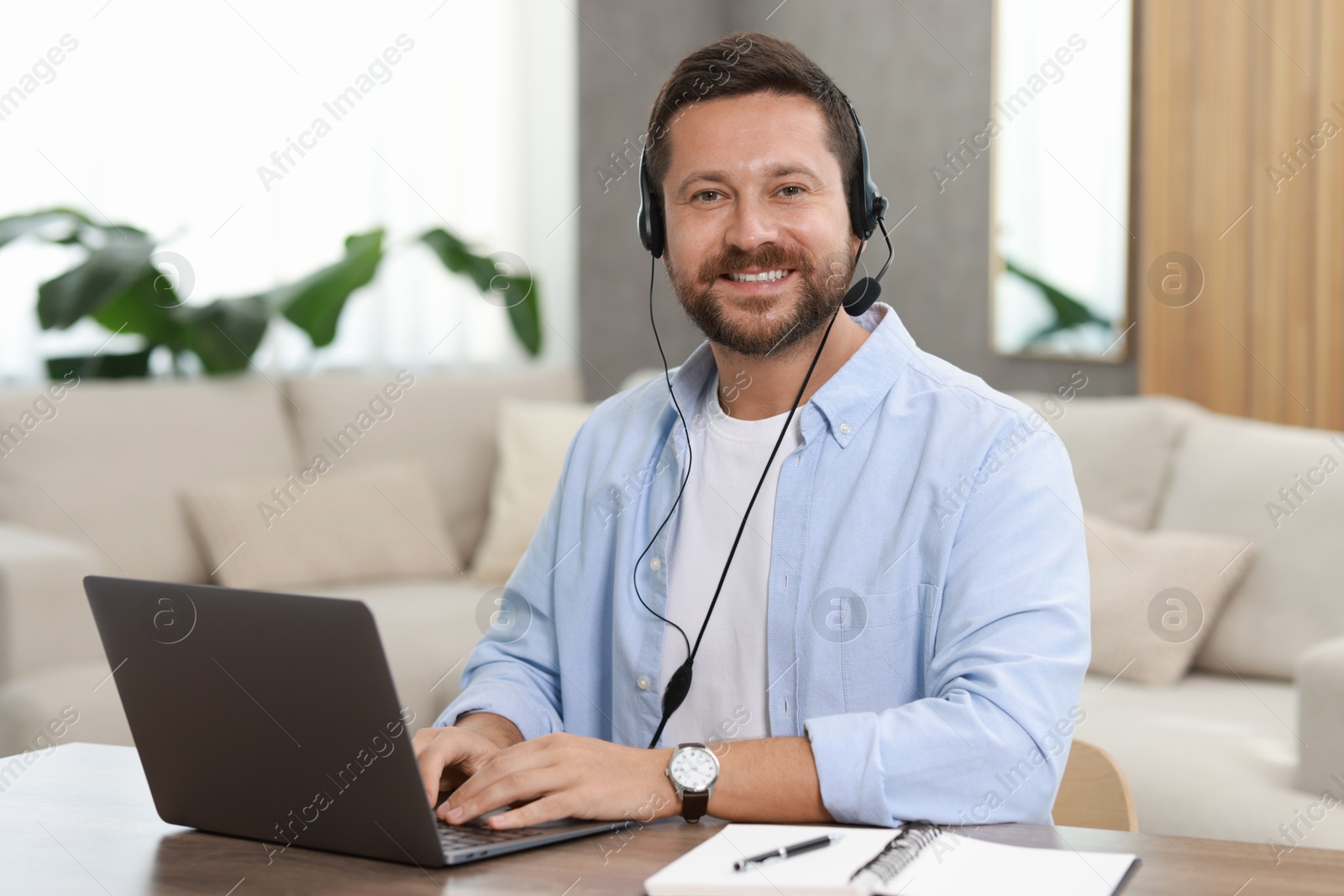 Photo of Interpreter in headset having video chat via laptop at wooden table indoors