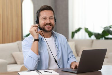 Interpreter in headset having video chat via laptop at wooden table indoors