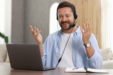 Interpreter in headset having video chat via laptop at wooden table indoors