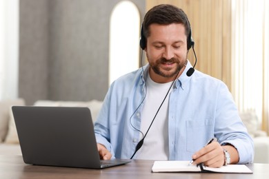 Photo of Interpreter in headset taking notes while having video chat via laptop at wooden table indoors