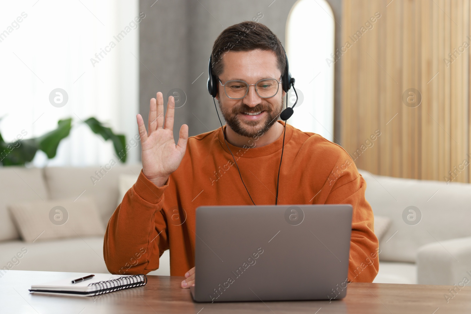 Photo of Interpreter in headset having video chat via laptop at wooden table indoors