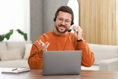 Photo of Interpreter in headset having video chat via laptop at wooden table indoors