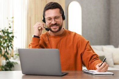 Interpreter in headset taking notes while having video chat via laptop at wooden table indoors