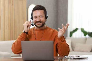 Photo of Interpreter in headset having video chat via laptop at wooden table indoors