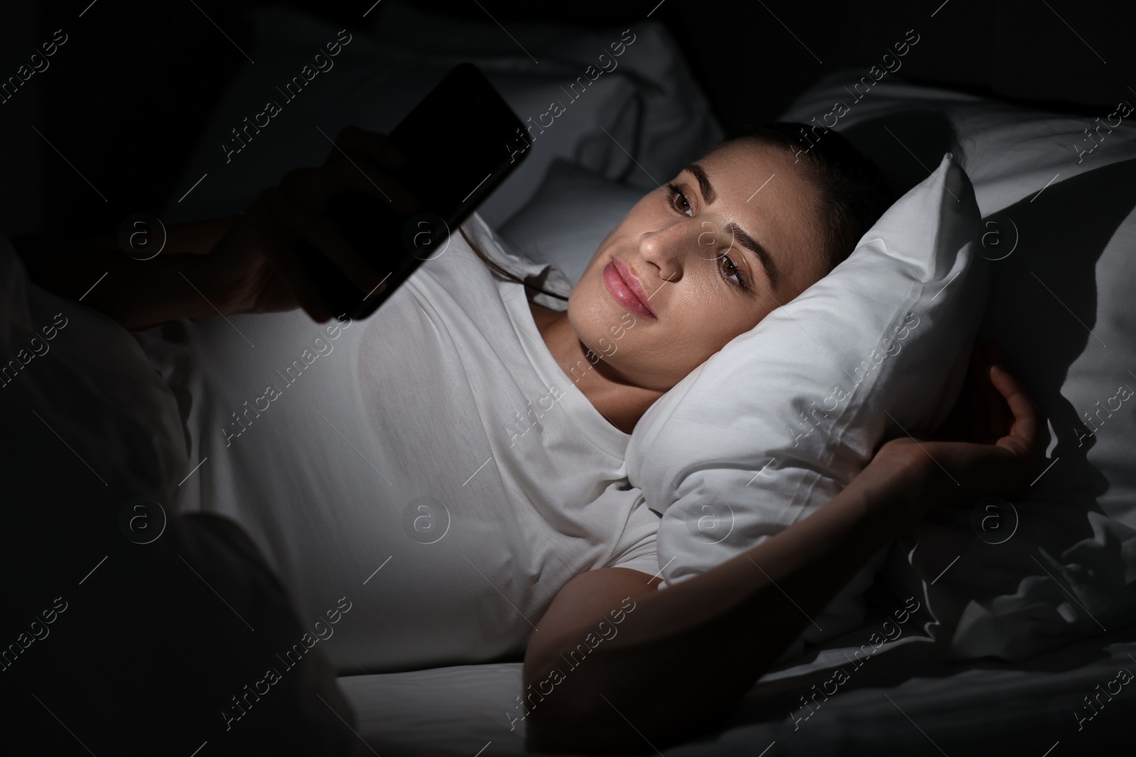 Photo of Bad habit. Young woman using smartphone in bed at night