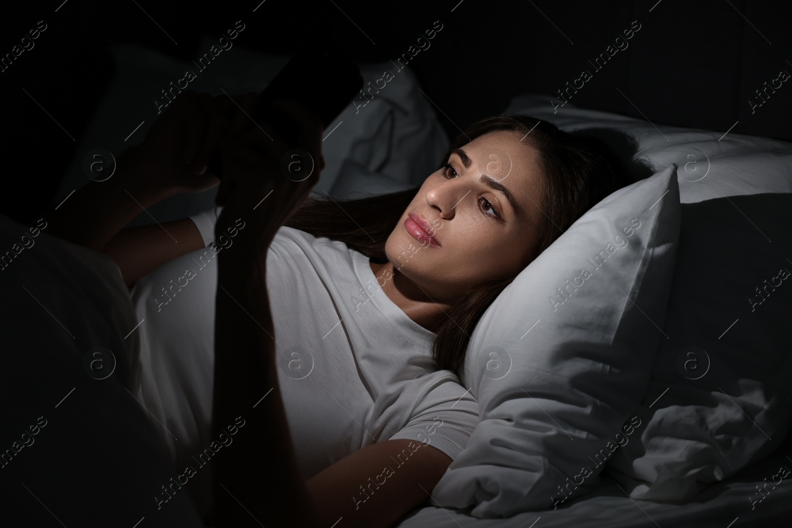 Photo of Bad habit. Young woman using smartphone in bed at night