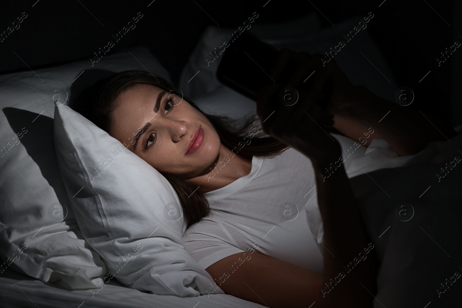 Photo of Bad habit. Young woman using smartphone in bed at night