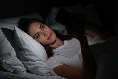 Photo of Bad habit. Young woman using smartphone in bed at night