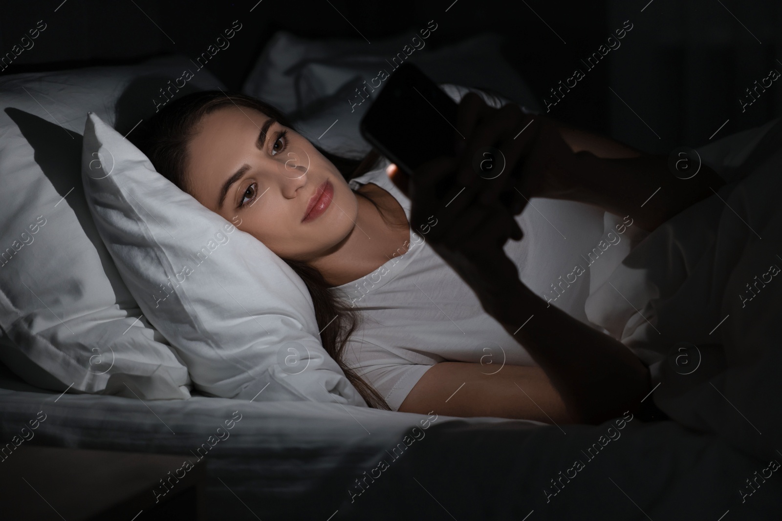 Photo of Bad habit. Young woman using smartphone in bed at night