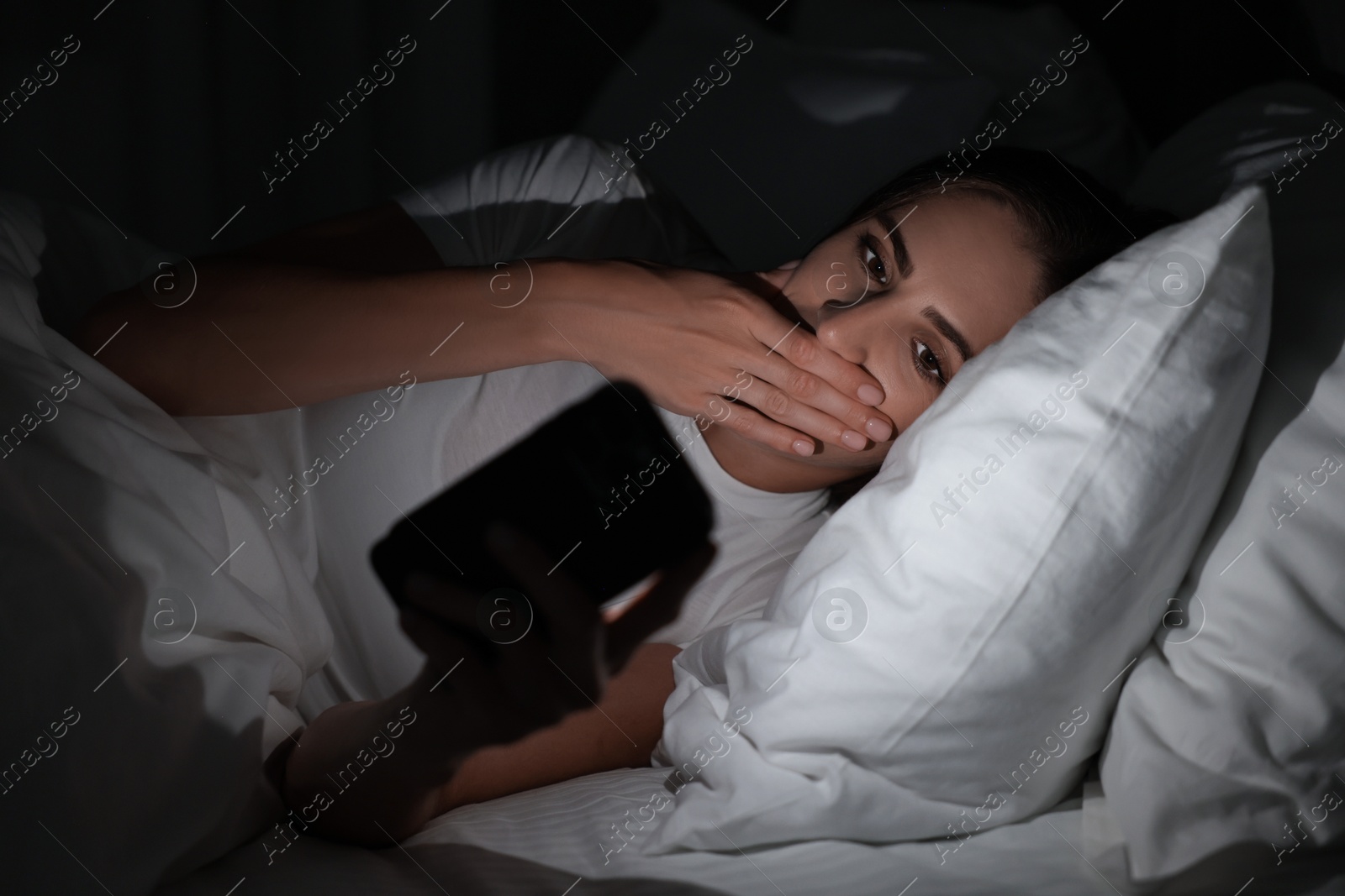 Photo of Bad habit. Young woman using smartphone in bed at night