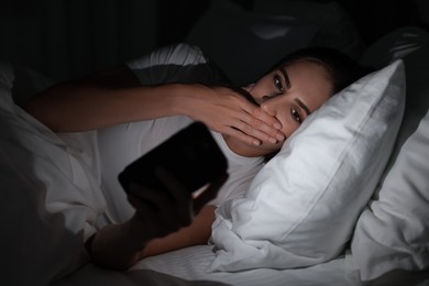 Photo of Bad habit. Young woman using smartphone in bed at night