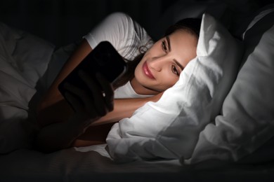 Photo of Bad habit. Young woman using smartphone in bed at night