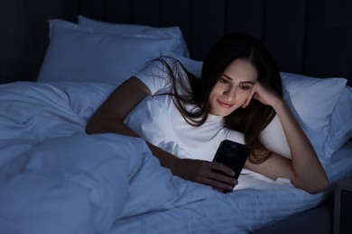 Photo of Bad habit. Young woman using smartphone in bed at night