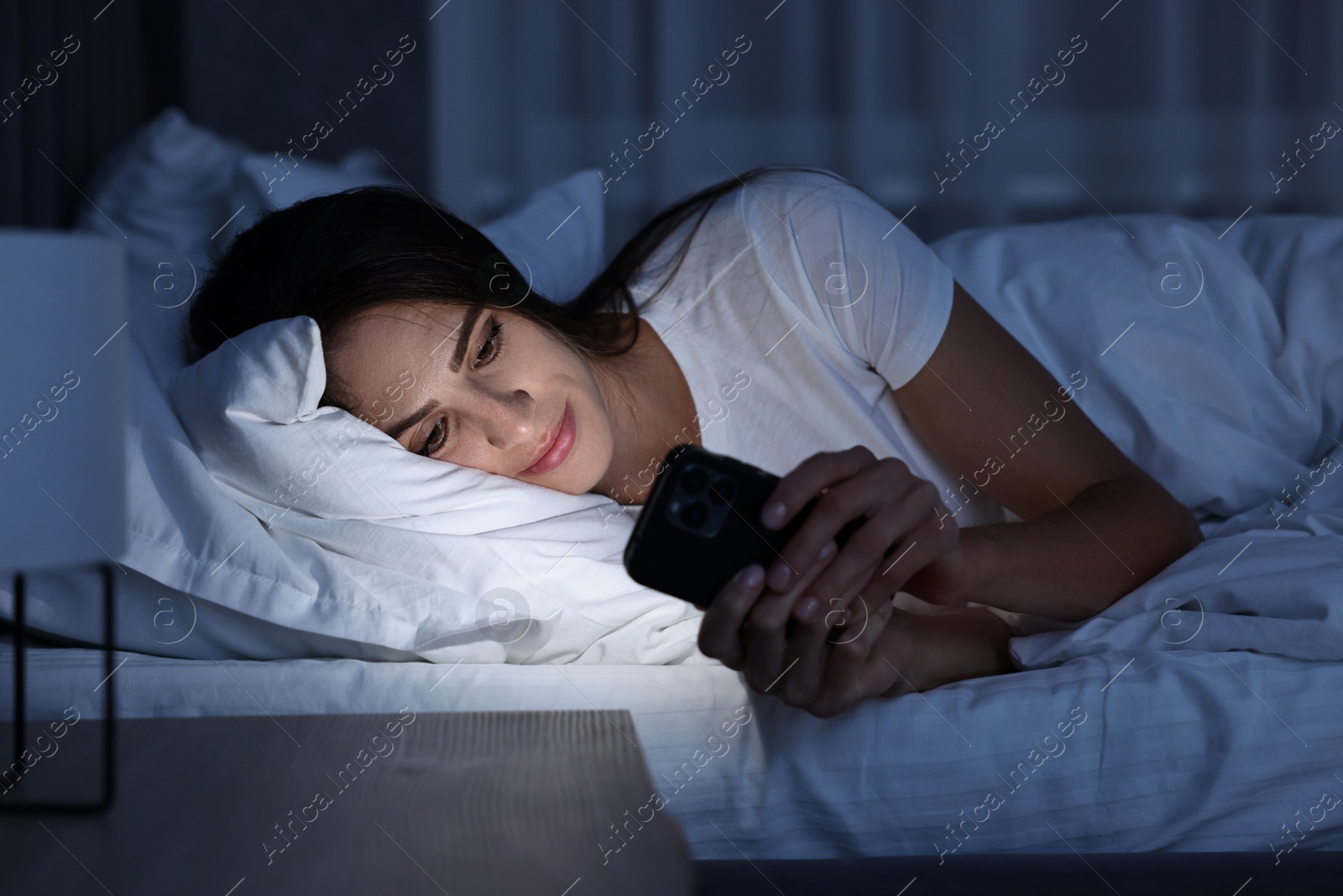 Photo of Bad habit. Young woman using smartphone in bed at night